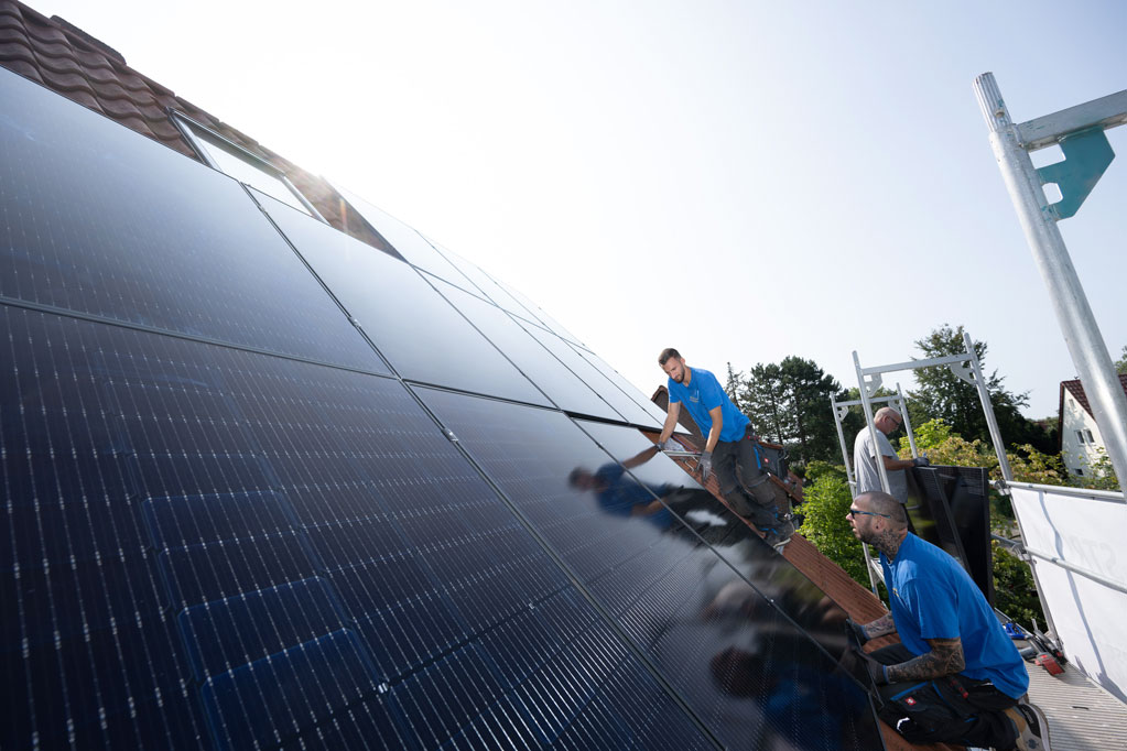 Mehrere Handwerker installierern Solarmodule auf einem Einfamilienhaus